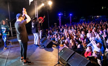 Band playing on stage with crowd in the background.